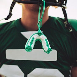 Green athletic mouthguard hanging from football helmet