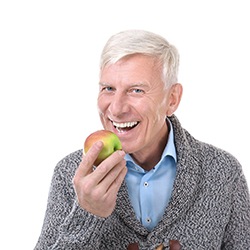 Older man in sweater eating an apple 