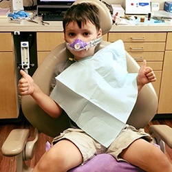Little boy in dental chair with nitrous oxide mask gives thumbs up