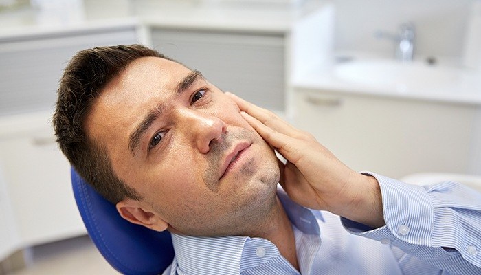Man in dental chair holding jaw in pain