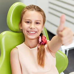 Young girl in dental chair giving thumbs up