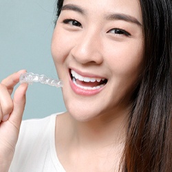 person holding a pair of Invisalign aligners in Sweeny and smiling