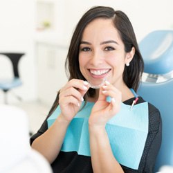 Smiling patient holding clear aligner in treatment chair