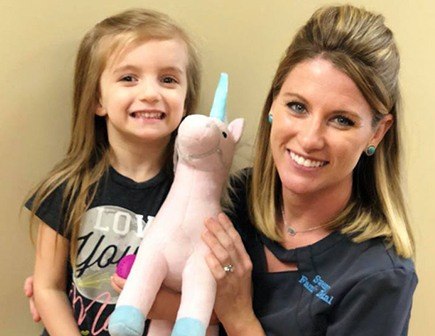 Team member smiling with young girl holding unicorn toy