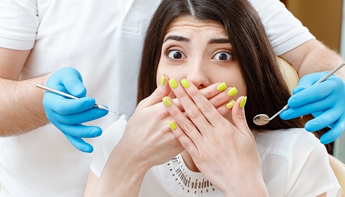 Frightened woman in dental chair covering mouth