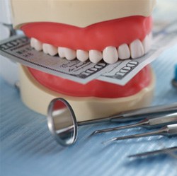 A jaw mockup biting dollar bills next to dental tools