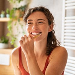 Woman smiling while brushing her teeth in bathroom