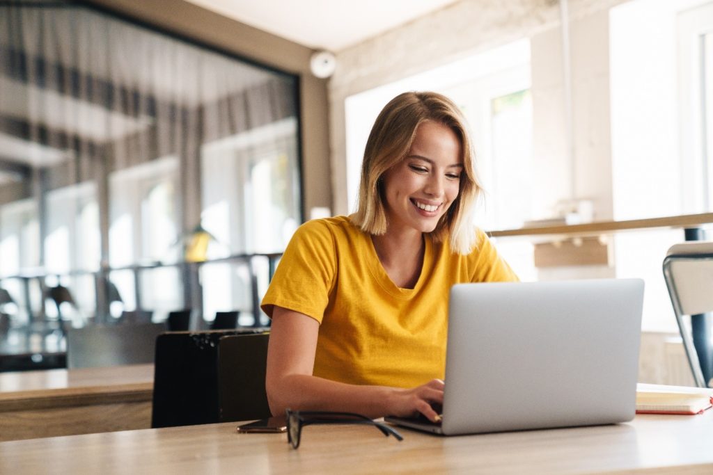 Woman in yellow shirt smiling while looking at laptop